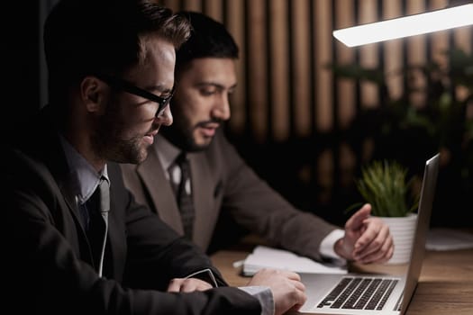 Two men discussing company growth, looking at rising graph on laptop screen