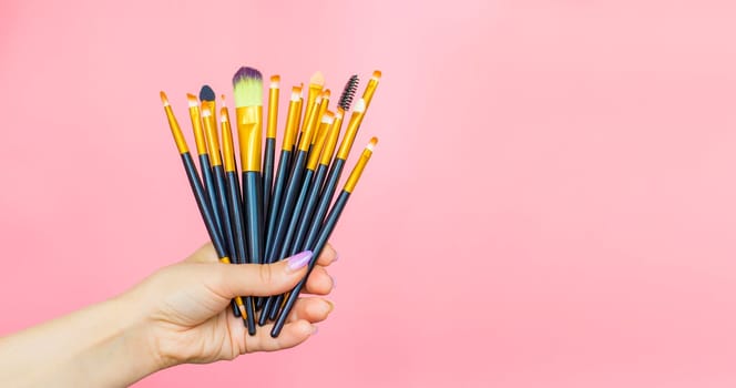 hand holding 15 Makeup Brushes Set, on pink background. beauty cosmetic product layout. woman Stylish design background. Creative fashion concept. Cosmetics make-up collection. makeup artist tools