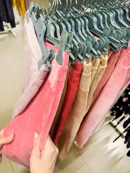 hand holds colorful pants on hangers in store. pants in shop. woman choosing new trousers in clothes store. Hands touch the corduroy trousers lying on the counter. shopping. clothing sale concept