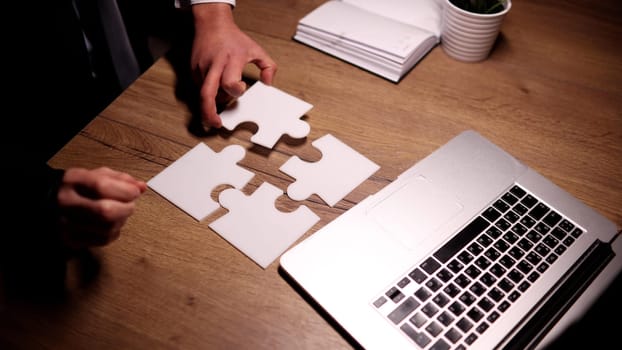 Close up focused young businessman putting puzzles together, finding difficult problem solution or involved in company growth strategy development