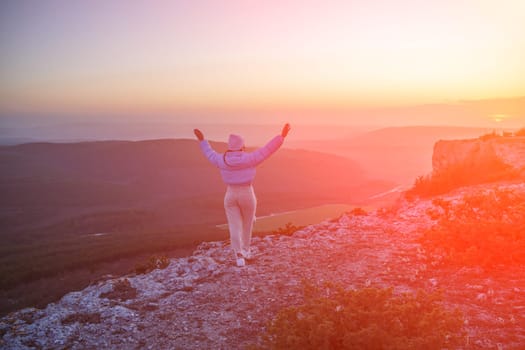 Woman hiker open arms on top of sunrise mountain. The girl salutes the sun, wearing a blue jacket, white hat and white jeans. Conceptual design