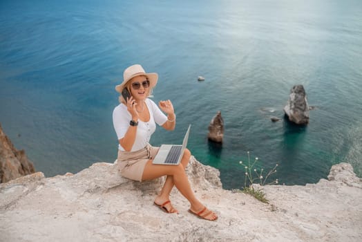 Freelance women sea working on the computer. Good looking middle aged woman typing on a laptop keyboard outdoors with a beautiful sea view. The concept of remote work