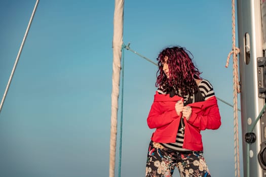 Woman standing on the nose of the yacht at a sunny summer day, breeze developing hair, beautiful sea on background.