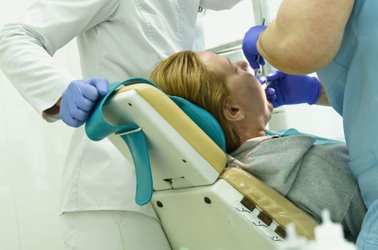 The dentist treats the teeth of the patient in the clinic. Close-up of the face, gloved hands, tools for dental treatment.