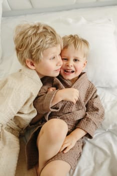 Boys, brothers lie on the bed in dressing gowns, play.