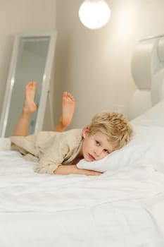 Portrait of a boy in a bathrobe, who lies on the bed and looks at the camera. Vertical frame.