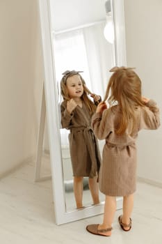A girl in a brown coat looks through a large mirror at the camera.