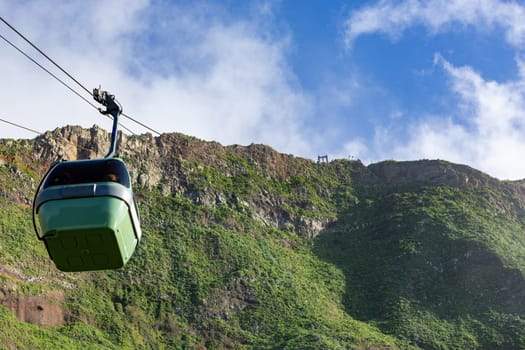 A cablecar in an idyllic mountain setting, with lush green pine trees and bushes in the foreground