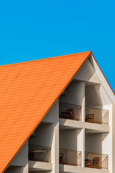 Geometric modern building facade exterior with orange tiled roof. Hotel against a blue sky.