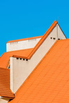 Geometric modern building facade exterior with orange tiled roof. Hotel against a blue sky.