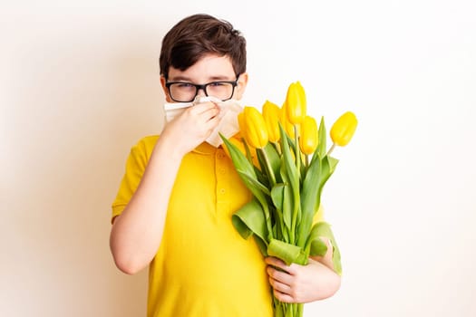 a brunette boy , dressed in a yellow T-shirt, holds a bouquet of yellow tulips and covered his nose with a paper napkin , look at camera, on a white background. To close up.