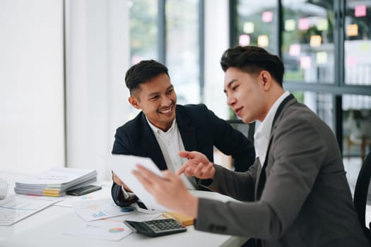 Two business men meeting to talking or discuss marketing work in workplace using paperwork, calculator, computer to work