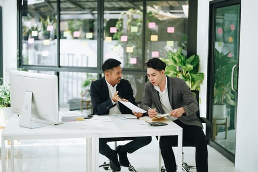 Two business men meeting to talking or discuss marketing work in workplace using paperwork, calculator, computer to work