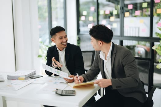 Two business men meeting to talking or discuss marketing work in workplace using paperwork, calculator, computer to work