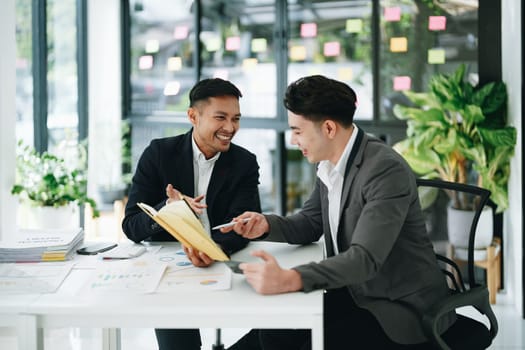 Two business men meeting to talking or discuss marketing work in workplace using paperwork, calculator, computer to work