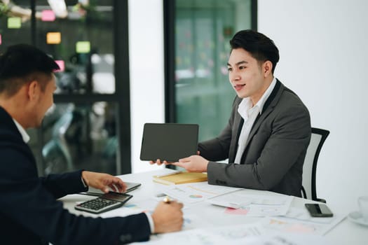 Two business men meeting to talking or discuss marketing work in workplace using paperwork, calculator, computer to work