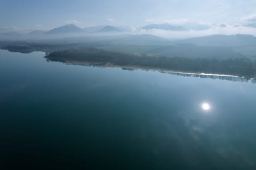 Morning sunrise over blue lake and misty forest. View from the top of the beautiful morning nature. A beautiful panoramic view of the lake and the forest, the trees are covered with fog.