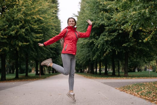 Young caucasian woman girl with toothy smile jumping in park forest outdoors looking at camera.