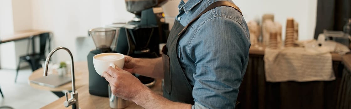 Handsome barista holding cup of coffee before giving to client while standing behind counter