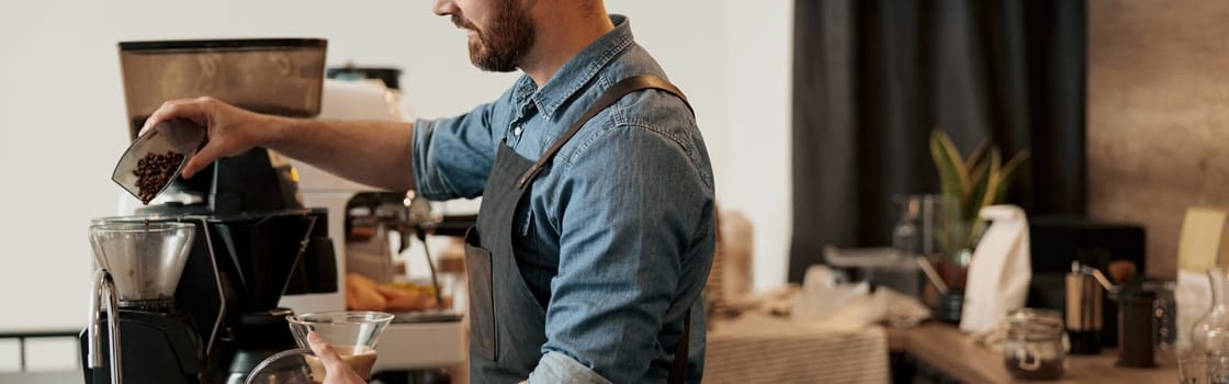 Barista pours coffee beans into the coffee machine tank for grinding standing behind counter