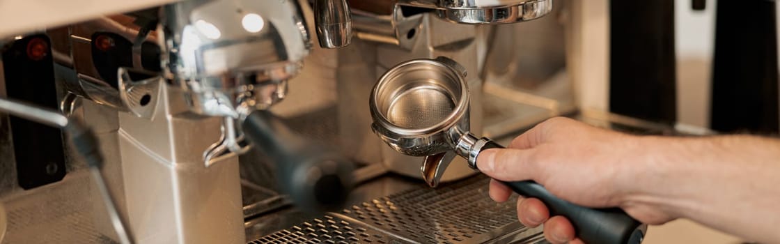 Close-up photo of hands of male barista installing filter with pressed coffee into coffee machine