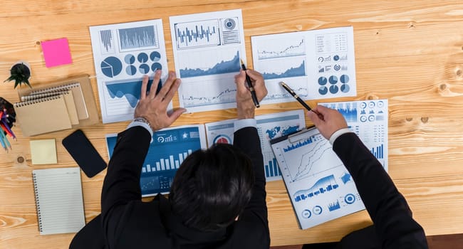 Top view analyst team discussing financial data on digital dashboard, analyzing chart and graph papers by data science software on wooden table background. Business intelligence and Fintech. Fervent