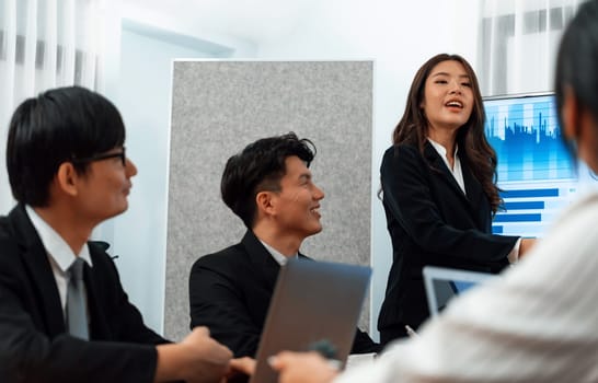 Confidence and young asian businesswoman give presentation on financial business strategy in dashboard report display on screen to colleagues in conference room meeting as harmony in workplace concept