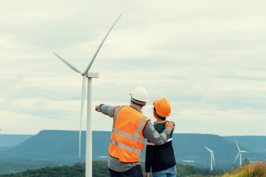 Engineer with his son on a wind farm atop a hill or mountain in the rural. Progressive ideal for the future production of renewable, sustainable energy. Energy generation from wind turbine.