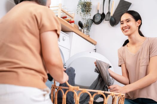 Daughter and mother working together to complete their household chores near the washing machine in a happy and contented manner. Mother and daughter doing the usual tasks in the house.