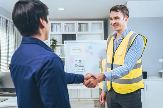 An engineer with a protective vest handshake with an investor in his office. Following a successful meeting, employee and employer form a partnership.