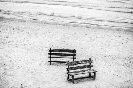 Two wooden benches stand on the beach with sand. A place of rest, reflection and solitude