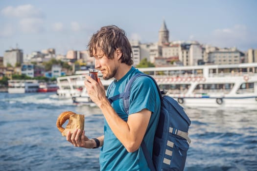 Man in Istanbul having breakfast with Simit and a glass of Turkish tea. Glass of Turkish tea and bagel Simit against golden horn bay and the Galata Tower in Istanbul, Turkey. Turkiye.