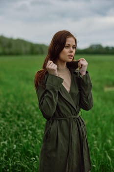 a beautiful woman stands in a green field and adjusts her coat. High quality photo