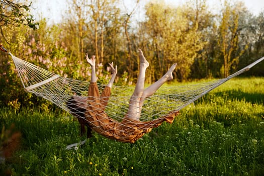 a funny woman is resting in nature lying in a mesh hammock in a long orange dress lifting up her arms and legs. High quality photo