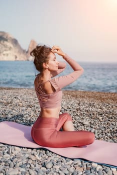 Young woman with long hair in white swimsuit and boho style braclets practicing outdoors on yoga mat by the sea on a sunset. Women's yoga fitness routine. Healthy lifestyle, harmony and meditation