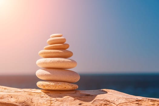 Balanced Pebbles Pyramid on the Beach on Sunny Day and Clear Sky at Sunset. Blue Sea on Background Selective focus, zen stones on sea beach, meditation, spa, harmony, calm, balance concept.