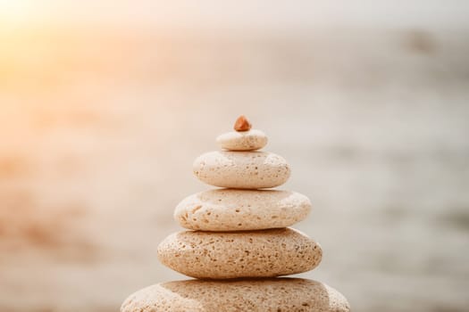 Pyramid stones on the seashore with warm sunset on the sea background. Happy holidays. Pebble beach, calm sea, travel destination. Concept of happy vacation on the sea, meditation, spa, calmness.