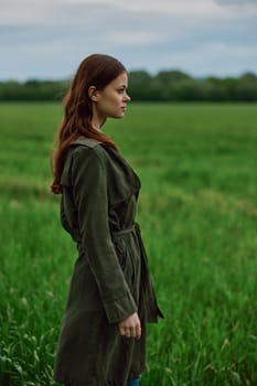 a beautiful, red-haired girl in a raincoat stands in a field in the spring in rainy weather. High quality photo