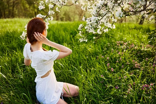 a woman in a light dress sits with her back to the camera near a flowering apple tree. High quality photo