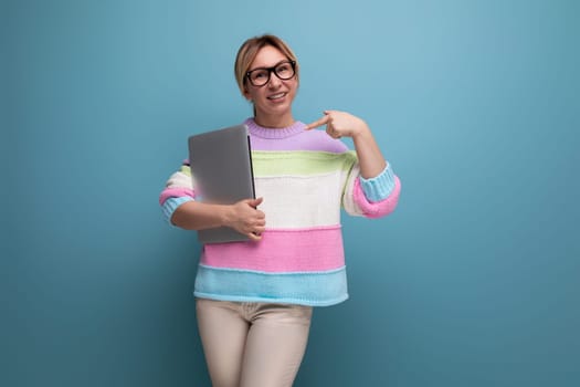 photo of a successful blond female freelancer in a striped sweater with a laptop on a blue background with copy space.