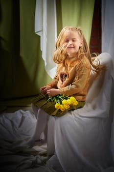 Portrait of a little blonde girl with bouquet of spring yellow flowers on a light background. Child in green dress holding a bouquet of tulips in hands. Spring concept