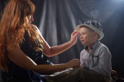 Woman with boy in hat. Mom with son on a dark background. Family portrait with mother with red hair and boy having fun together