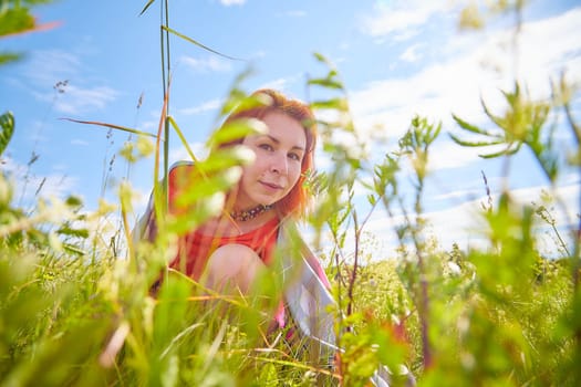 Outdoors portrait of red haired woman in grass and lower on field and meadow. Young woman enjoying her freedom in flowering nature