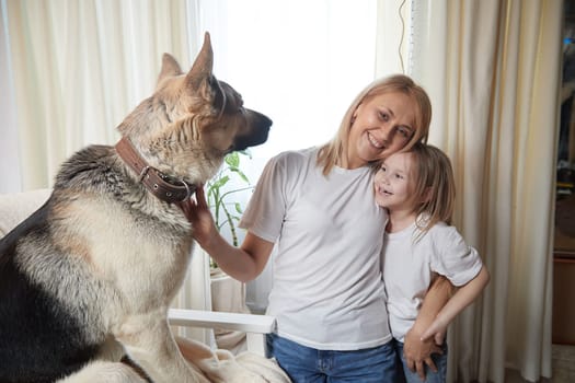 Happy loving family with mother, daughter and big dog in living room. Pet chephers, woman mom and small child girl who is afraid of a dog taken from a shelter