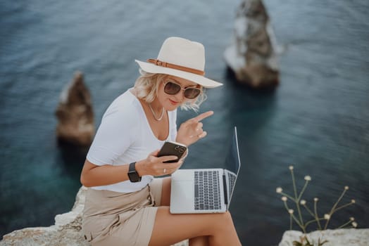 Freelance women sea working on the computer. Good looking middle aged woman typing on a laptop keyboard outdoors with a beautiful sea view. The concept of remote work