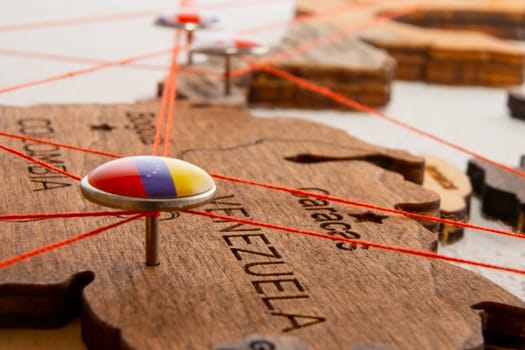 Venezuela flag on the pushpin and red threads on the wooden map. Travel or logistic routes. Influence in geopolitics and world economy.