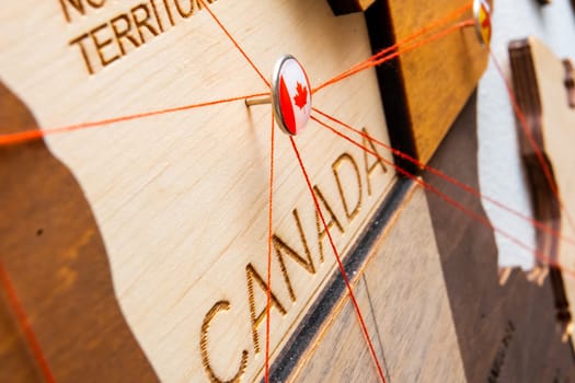 Canada flag on the pushpin and red threads on the wooden map. Travel or logistic routes. Influence in geopolitics and world economy.