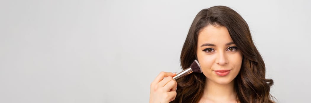 Portrait of beautiful young woman with makeup brush and natural makeup on the banner with grey background