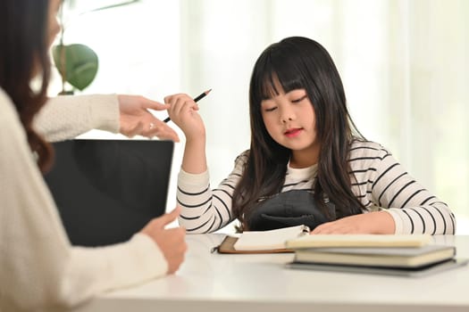 Cute little girl doing homework with tutor at home. Homeschooling and education concept.