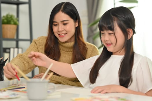 Caring young mother and little daughter doing homework, learning at home. Homeschooling concept.